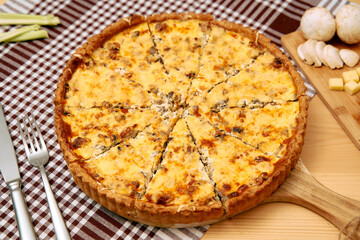 Mushroom and cheese quiche on wooden board with checkered tablecloth