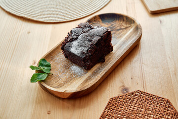 Rich chocolate brownie with powdered sugar on wooden plate in rustic setting