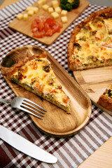 Delicious vegetable quiche slice on wooden plate with cheese and tomato garnish
