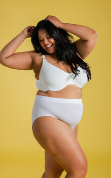 Female model smiling while running hands through hair in studio wearing underwire bra and briefs
