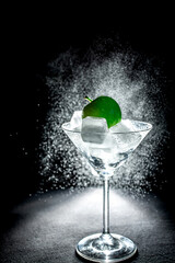 Fresh cocktail with green apple and ice cubes in a martini glass on black background
