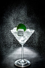 Fresh cocktail with green apple and ice cubes in a martini glass on black background
