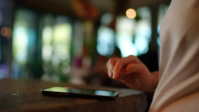 Young woman at restaurant, intently browsing smartphone screen, scrolling and tapping digital content with focused finger movements, blurred background creating soft light ambiance