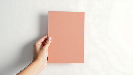 Obraz premium Woman's hand holding a peach-colored flyer mockup; minimalist, clean design, elegant branding.