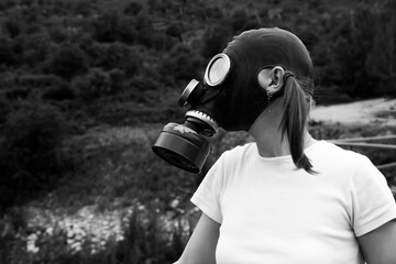 A woman in a gas mask stands outdoors, looking to the side, surrounded by nature