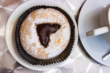 A fresh cup of cappuccino in a white ceramic mug served with a chocolate filled pastry topped with...