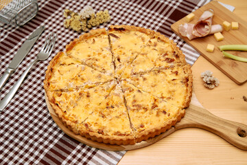 Savory cheese and bacon quiche on wooden board with checked tablecloth and flower decor