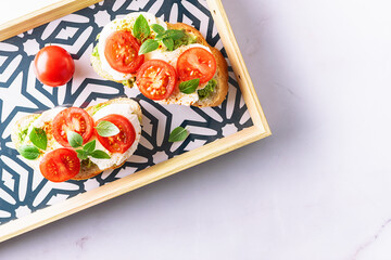 Fresh homemade caprese sandwich with avocado paste, mozzarella cheese, cherry tomatoes, fresh aromatic basil leaves and spicy hot oil on bright serving board top view. Healthy homemade food concept.