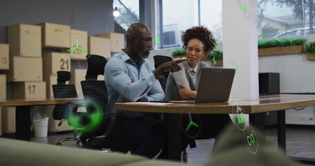 Collaborating colleagues presenting sustainability metrics on laptop in office, green icons
