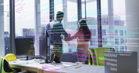 Design professionals examining blueprint in high-rise office, with hard hat and monitors