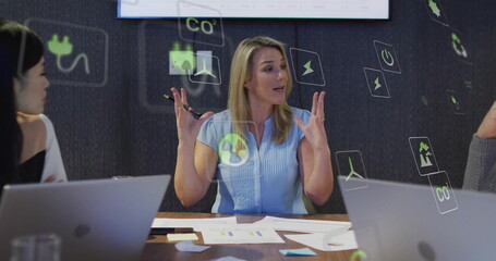 Leading discussion mature female raising hands, holding pen in boardroom with holographic icons