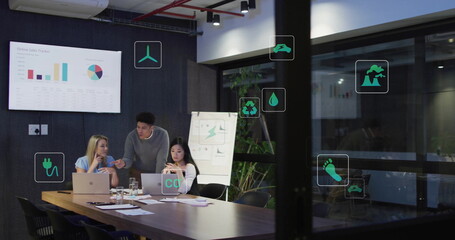 Analyzing team wearing business attire reviewing charts at meeting table, with laptops, eco icons