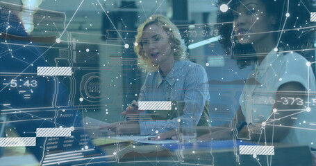 Gesturing blonde woman explaining network overlay at conference table, with pen, documents, monitor