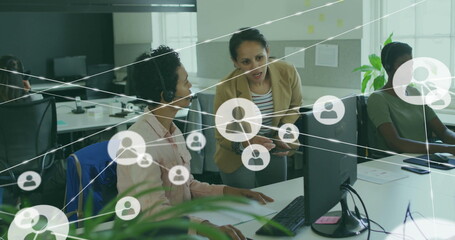 Leaning supervisor guiding seated agent at open office, with computer headsets showing teamwork
