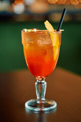 Refreshing orange cocktail in glass with lemon garnish and black straw on wooden table
