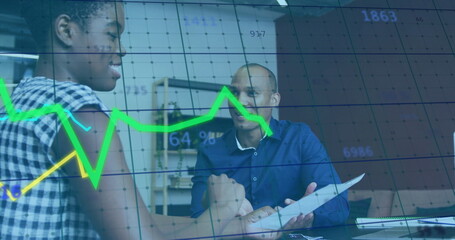 Analyzing colleagues in business attire reviewing data in office meeting, with reports and charts