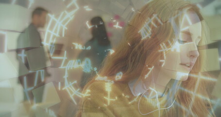 Woman wearing headphones and mustard sweater analyzing interface graphics in office, with panel