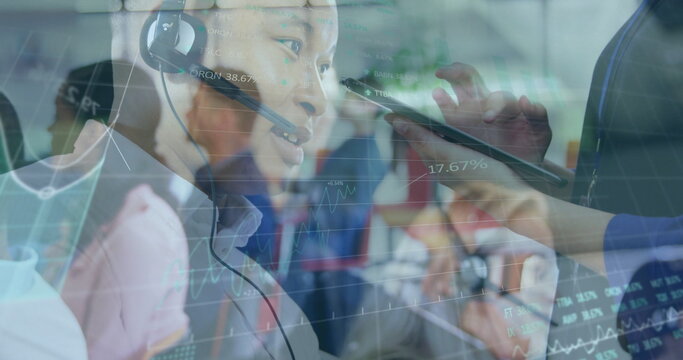Asian man wearing headset and shirt talking in office call center, with stylus pointing at tablet - Powered by Adobe