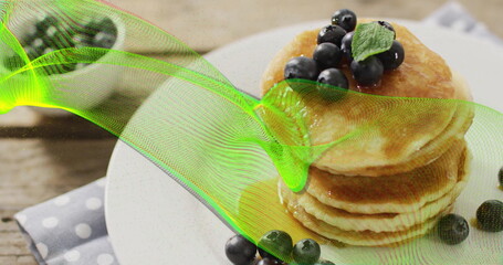 Showcasing stack of golden pancakes on wooden table, with blueberries, mint leaf and neon overlay © vectorfusionart