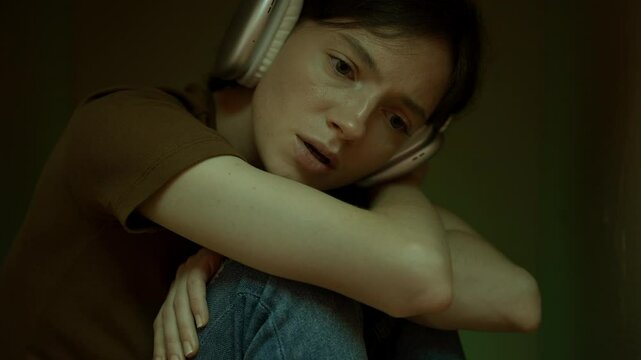 Young teenage girl listening to music on headphones sitting in a cardboard box closed off from the outside world. Depression and loneliness