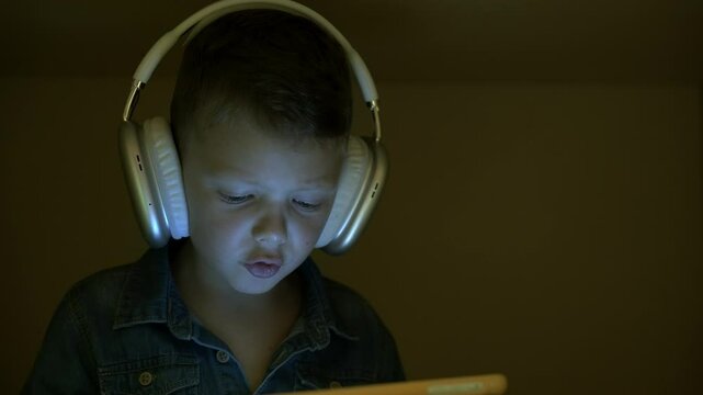 Concept of loneliness. Little boy playing game on tablet sitting inside cardboard box.