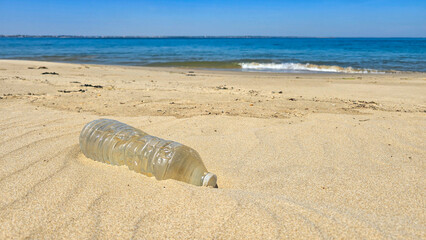 A plastic bottle lies on a clean sandy beach on the seashore or ocean. The danger of plastic...