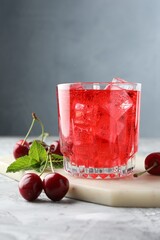 Tasty cherry soda with ice cubes, berries and mint in glass on grey textured table, closeup
