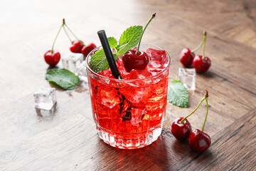 Tasty cherry soda with ice cubes, berries and mint in glass on wooden table, closeup