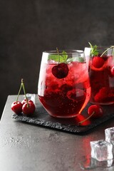 Tasty cherry soda with ice cubes, berries and mint in glasses on grey table, closeup