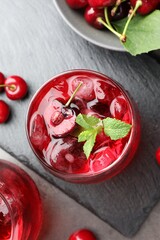 Tasty cherry soda with ice cubes, berries and mint in glasses on grey table, flat lay