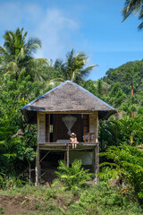 Surrounded by vibrant greenery, a woman enjoys a peaceful moment in a bamboo hut, savoring the natural beauty of the jungle. The atmosphere is serene and inviting, encouraging relaxation