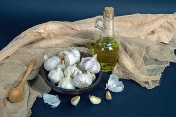 fresh garlic cloves in a clay bowl and garlic oil on a dark background