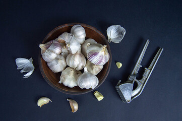 garlic in a clay bowl on a dark background with a garlic press