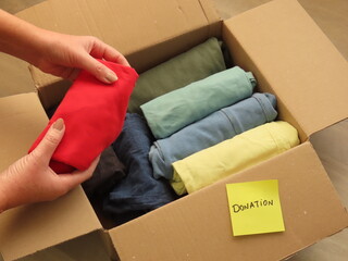 Woman hands preparing a box of clothes for donation. Sorting clothes for donation.