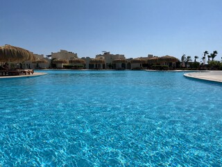Swimming pool with turquoise water. In the background are sun loungers and umbrellas of a luxury hotel, stunning summer view. Concept of rest, travel, tourism
