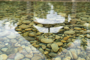 Clear water reveals round, smoothly polished stones. The light reflections dance on the surface.
