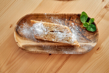 Powdered apple strudel slice with mint garnish on wooden plate