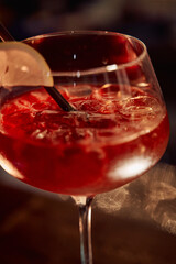 Refreshing red cocktail in glass with lemon slice and straw on dark background