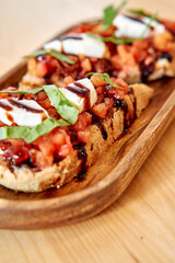 Fresh tomato bruschetta with mozzarella and basil drizzled with balsamic glaze on wooden board