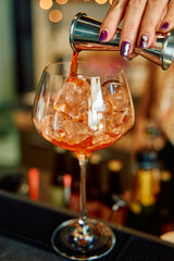 Jigger pouring aperol over ice in large wine glass for cocktail mixing