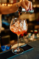 Bartender pouring aperol spritz into glass with ice at bar countertop