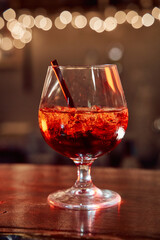 Sparkling red cocktail in snifter glass with straw under warm ambient lights
