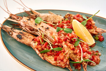 Grilled shrimp with tomato salsa and lemon on oval plate with microgreens garnish