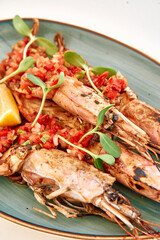 Grilled king prawns with tomato salsa and microgreens on ceramic plate with lemon wedge