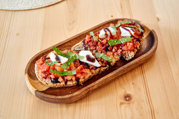 Rustic bruschetta with tomatoes basil and mozzarella on wooden platter
