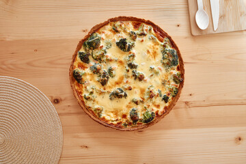 Delicious broccoli cheese quiche on wooden table with plate and cutlery