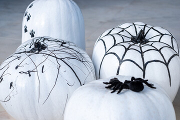 White pumpkins decorated with black spider webs, spiders, and intricate designs create a spooky...