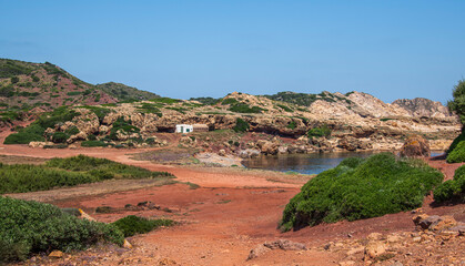 Secluded red sand beach framed by rocky hills, lone white building highlighting pristine coastal...