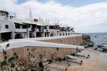 Whitewashed houses with dark accents perched on coastal hillside, overlooking turquoise waters of...
