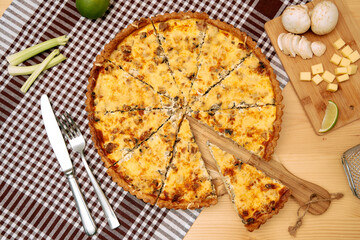 Cheese and mushroom quiche with cutting board and utensils on checkered cloth